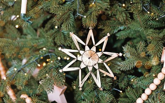 Decorative straw star ornament on a green Christmas tree adorned with lights