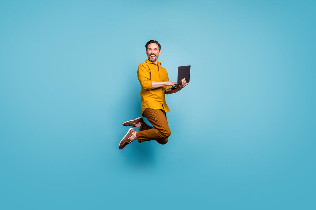 Full size photo of funky man feel rejoice emotions jump use laptop search social media online black friday discounts wear casual style clothing isolated over blue color background