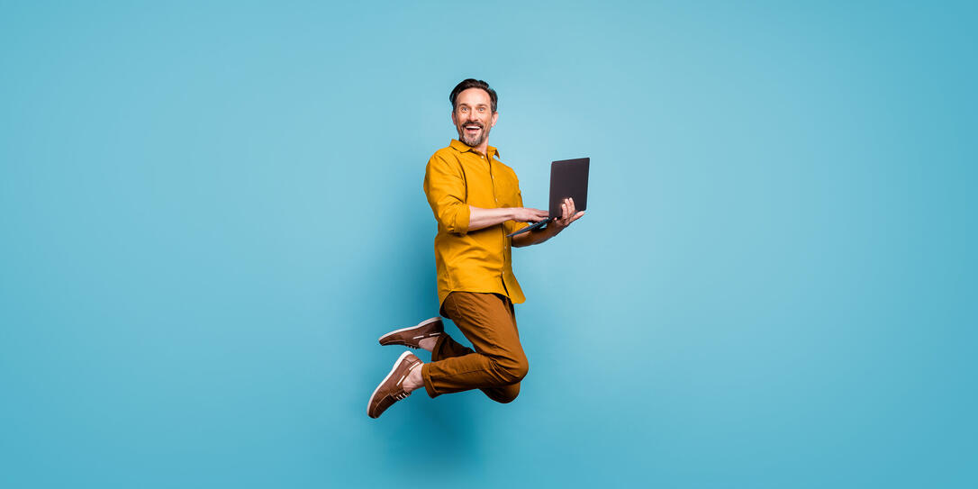 Full size photo of funky man feel rejoice emotions jump use laptop search social media online black friday discounts wear casual style clothing isolated over blue color background