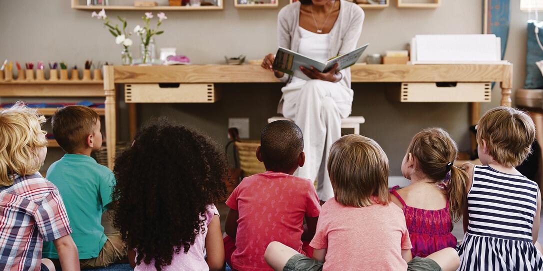 Teacher At Montessori School Reading To Children At Story Time