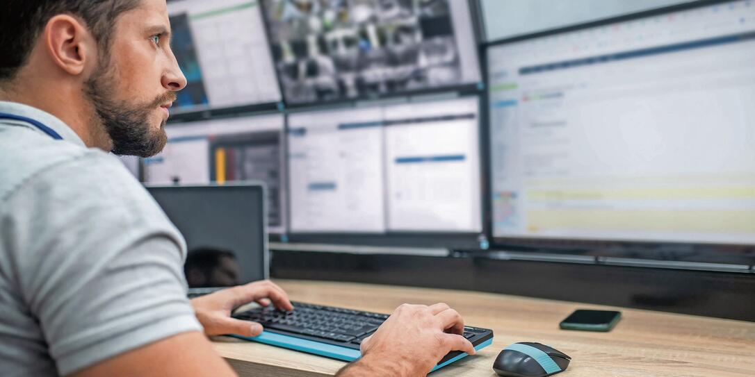 Attentive man with keyboard in front of computer screens