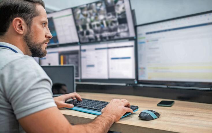 Attentive man with keyboard in front of computer screens