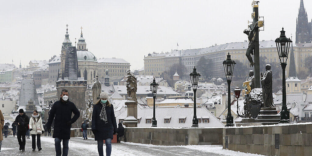 Menschen überqueren die mittelalterliche Karlsbrücke nach dem ersten Schneefall in Prag am ersten Tag der Lockerungen der Corona-Maßnahmen in Tschechien nach einem Lockdown. Am Donnerstag durften alle Geschäfte, Einkaufszentren, Restaurants, Bars und Hotels wieder öffnen. Foto: Petr David Josek/AP/dpa