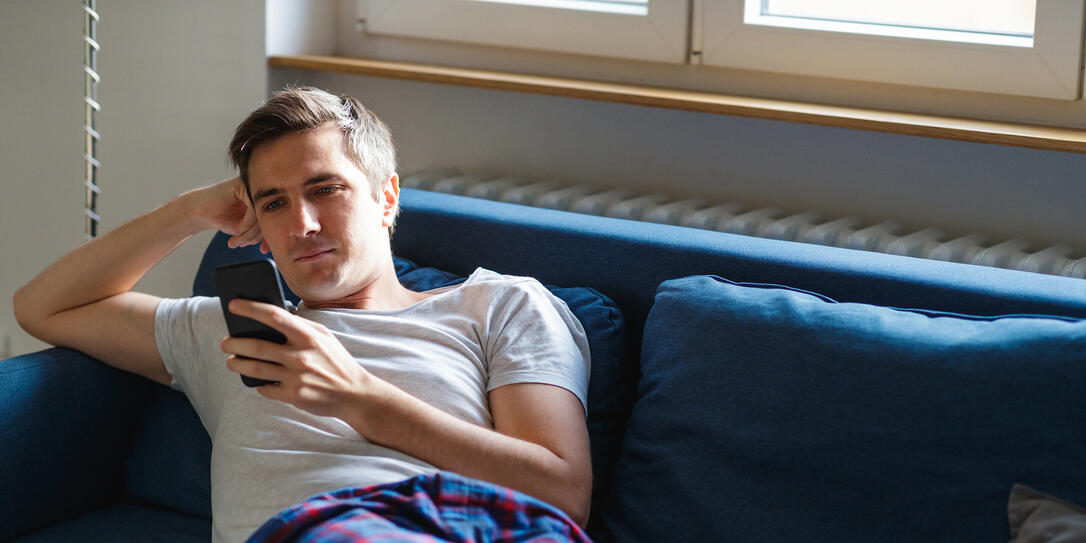 Young man on the sofa in pajamas checking smart phone Young man on the sofa in pajamas checking smart phone