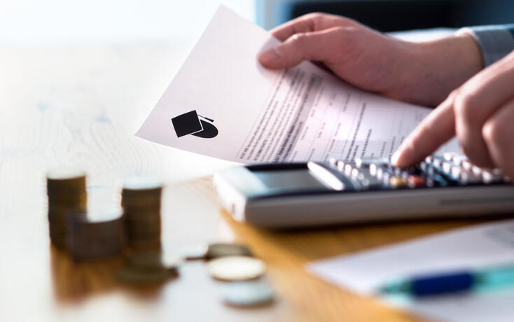 Man counting college savings fund, tuition fee or student loan with calculator. Education price and expenses concept. Money and papers on table.