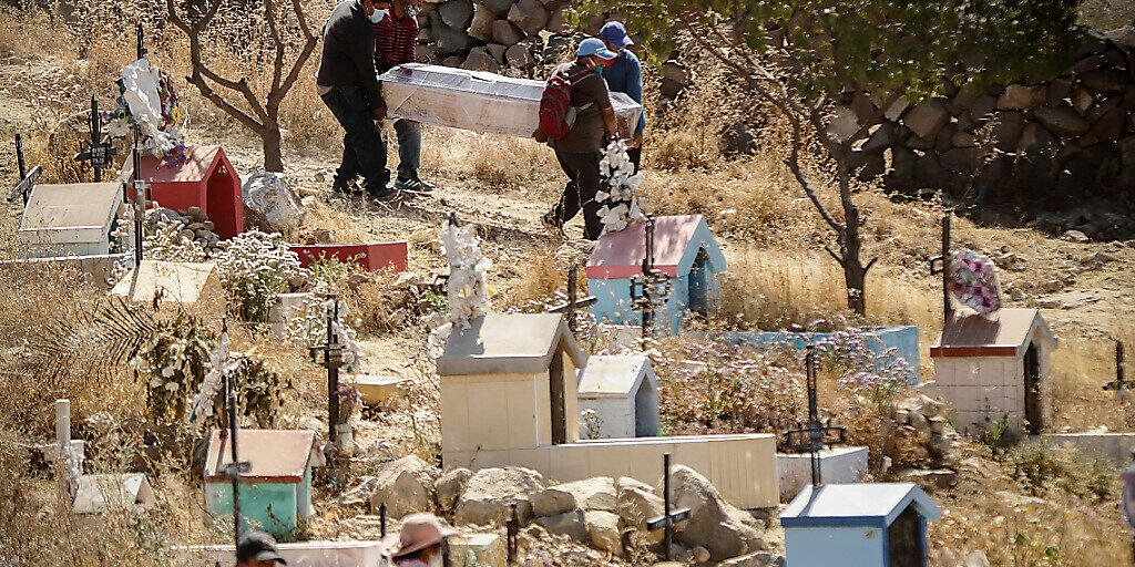 ARCHIV - Menschen mit Mundschutzmasken tragen inmitten der Corona-Pandemie einen Sarg bei einre Beerdigung auf dem Friedhof El Cebollar in Peru. Foto: Denis Mayhua/dpa