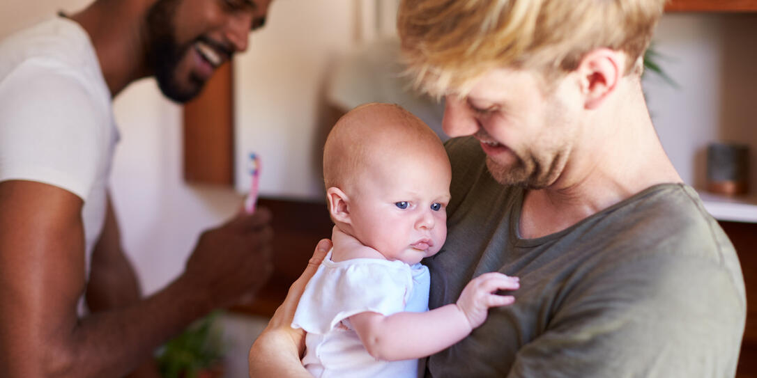 Loving Male Same Sex Couple Cuddling Baby Daughter In Bathroom At Home Together Loving Male Same Sex Couple Cuddling Baby Daughter In Bathroom At Home Together