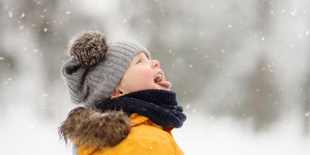 Cute little boy catching snowflakes with her tongue in beautiful winter park