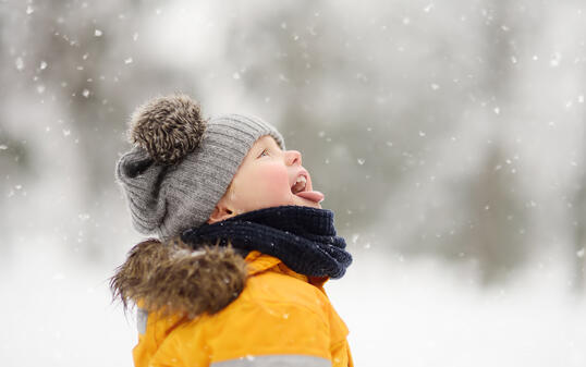 Cute little boy catching snowflakes with her tongue in beautiful winter park