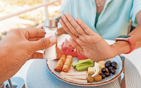 Woman in a restaurant refuses the offered salt and pepper shaker with a gesture of her hand. Diet for gout and high cardiovascular blood pressure