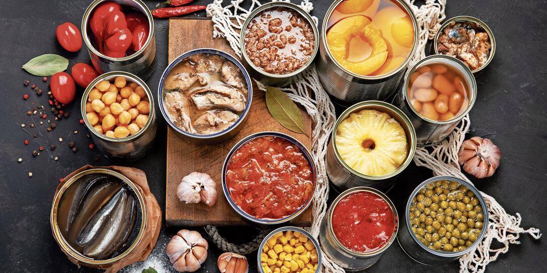 Canned vegetables, beans, fish and fruits in tin cans on black background. Food stocks.