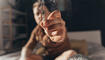 Man offering a hand rolled cannabis cigarette while sitting at the bed