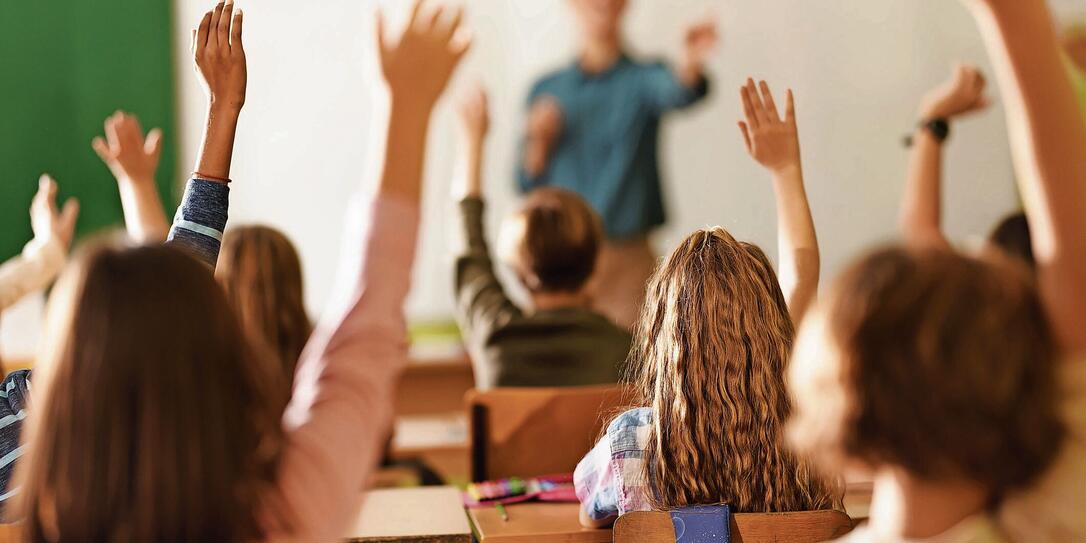 Back view of school kids raising their hands on a class in the classroom. Back view of school kids raising their hands on a class in the classroom.