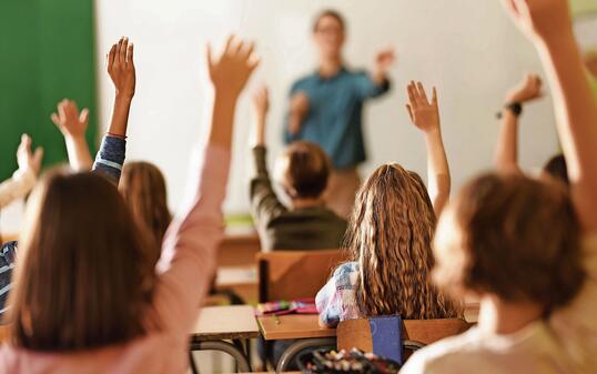 Back view of school kids raising their hands on a class in the classroom.