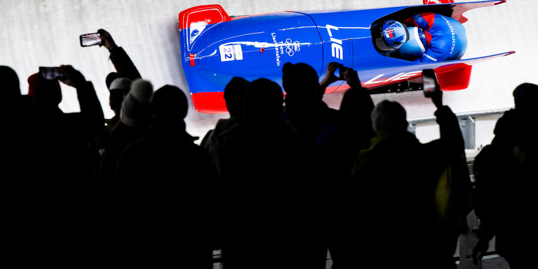 Spezielles Ambiente bei Flutlicht. Liechtensteins Zweierbob verfolgt von vielen Zuschauern.