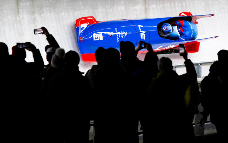 Spezielles Ambiente bei Flutlicht. Liechtensteins Zweierbob verfolgt von vielen Zuschauern.