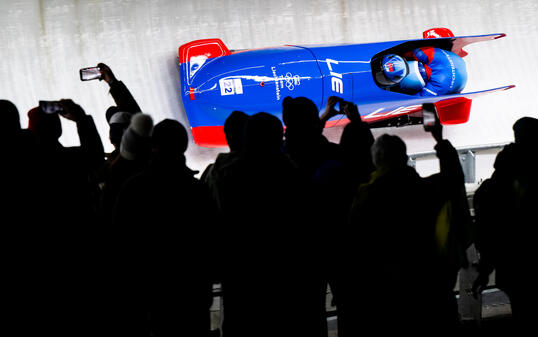 Spezielles Ambiente bei Flutlicht. Liechtensteins Zweierbob verfolgt von vielen Zuschauern.