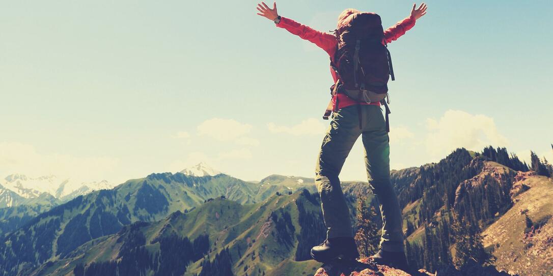 cheering successful woman backpacker open arms on mountain peak