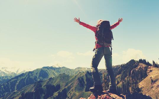 cheering successful woman backpacker open arms on mountain peak