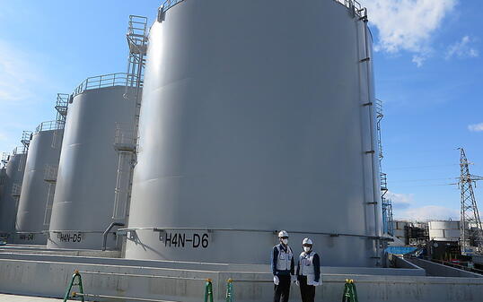 ARCHIV - Mitarbeiter des Betreiberkonzerns Tepco stehen vor riesigen Tanks, in denen verstrahltes Wasser, das bei der andauernden Kühlung der beschädigten Reaktoren von Fukushima anfällt, gelagert wird. Inzwischen haben sich 1,1 Millionen Tonnen angehäuft, langsam geht der Platz für weitere Tanks aus. Foto: Lars Nicolaysen/dpa