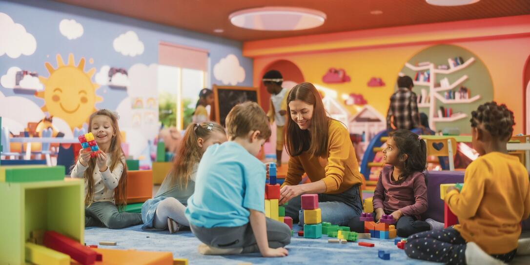 Cheerful Diverse Kids Playing with Colorful Building Block Toys in Kindergarten. Group of Multiethnic Boys and Girls Playing Together with a Female Teacher in a Modern Daycare Center