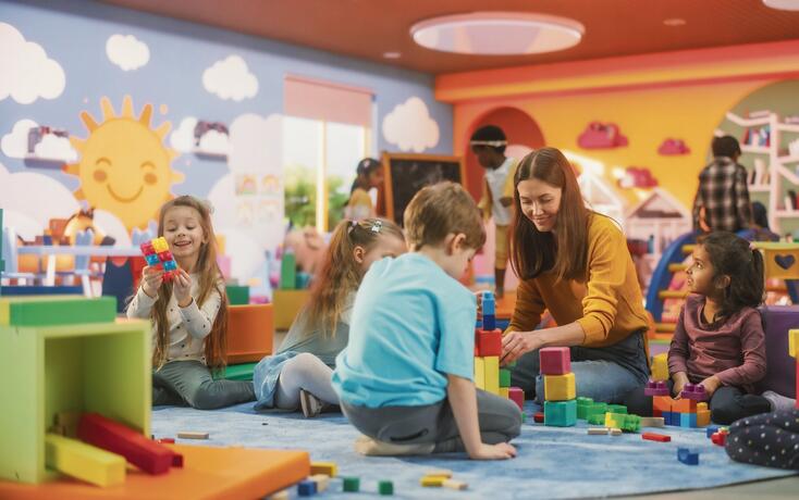 Cheerful Diverse Kids Playing with Colorful Building Block Toys in Kindergarten. Group of Multiethnic Boys and Girls Playing Together with a Female Teacher in a Modern Daycare Center