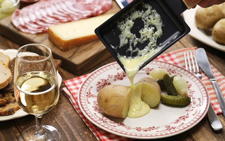 Raclette cheese melted by raclette pan is putting on freshly boiled potatoes.