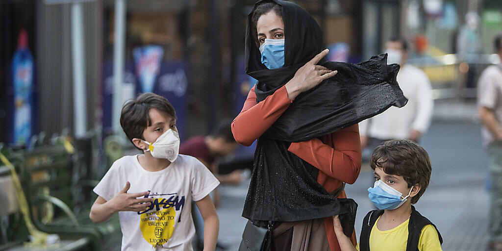 Kinder mit Gesichtsmasken gehen mit ihrer Mutter eine Straße entlang. Der Iran meldete am 21. Juli eine neue Rekordzahl an Corona-Toten. Foto: Ahmad Halabisaz/XinHua/dpa