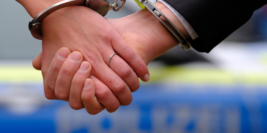 Young couple with hand-cuffs in front of a police car
