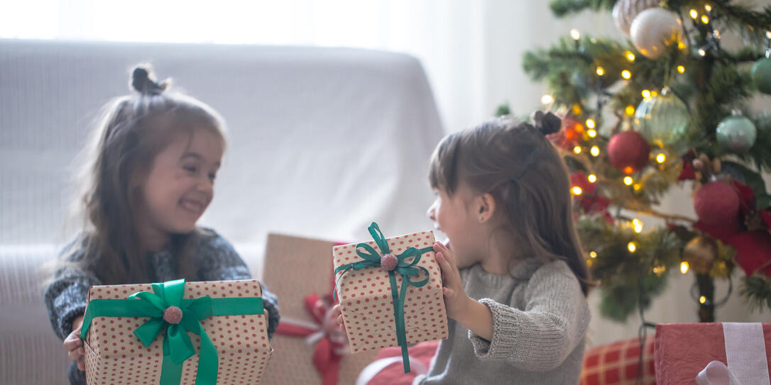 Pretty little girls are holding a gift boxes and smiling at home on light background Pretty little girls are holding a gift boxes and smiling at home on light background