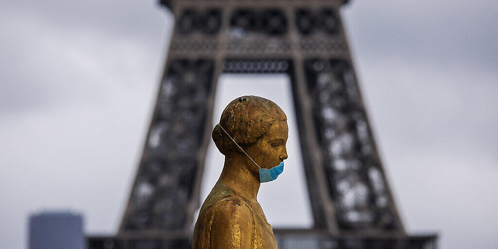 Eine goldene Statue am Pariser Platz Trocadéro trägt eine Schutzmaske. Im Hintergrund ist das berühmte Wahrzeichen Eiffelturm zu sehen. (Archivbild) Eine goldene Statue am Pariser Platz Trocadéro trägt eine Schutzmaske. Im Hintergrund ist das berühmte Wahrzeichen Eiffelturm zu sehen. (Archivbild)