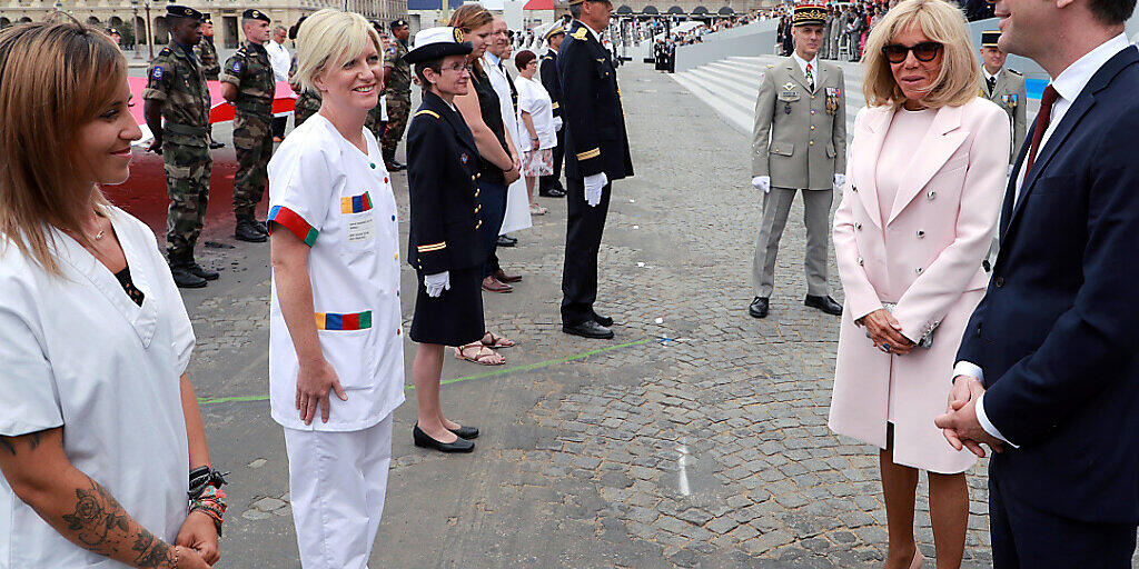 Olivier Veran (r), Gesundheitsminister von Frankreich, und Brigitte Macron (2.v.r), Ehefrau von Frankreichs Präsident Macron, reden mit medizinischem Personal am Ende der Militärfeier zum Nationalfeiertag. Foto: Ludovic Marin/AFP/AP/dpa