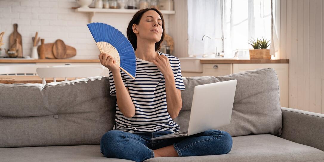 Young woman suffers from heatstroke flat without air-conditioner waving fan sitting on couch at home