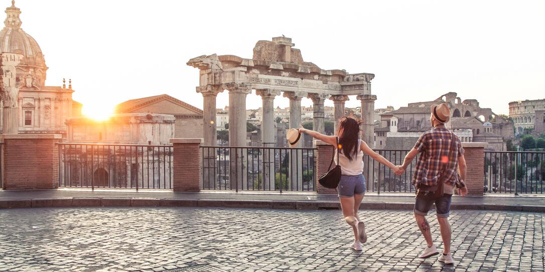 Young couple tourist walking pointing towards Roman Forum at sunrise. Historical imperial Foro Romano in Rome, Italy from panoramic point of view.