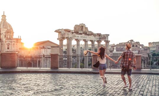Young couple tourist walking pointing towards Roman Forum at sunrise. Historical imperial Foro Romano in Rome, Italy from panoramic point of view.