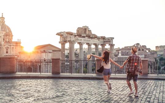 Young couple tourist walking pointing towards Roman Forum at sunrise. Historical imperial Foro Romano in Rome, Italy from panoramic point of view.