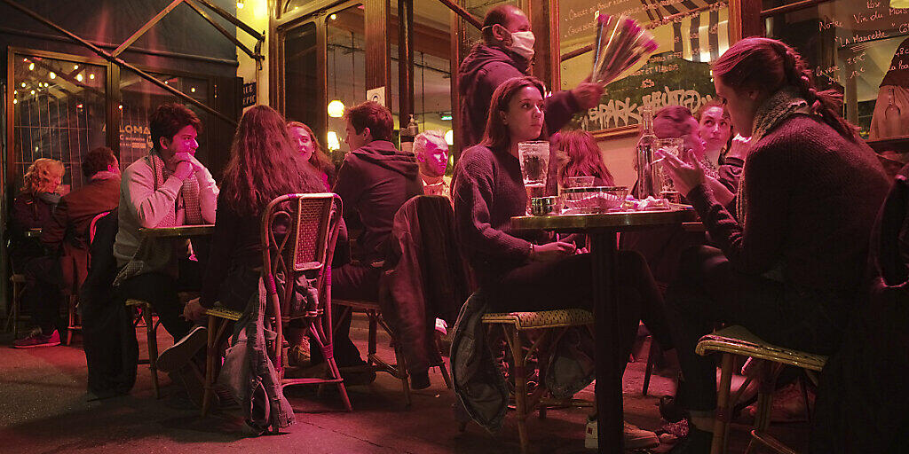 Menschen sitzen an Tischen auf einer Caféterrasse in Paris. Erneut gibt es Einschränkungen bei den Öffnungszeiten von Bars und Restaurants. Foto: Lewis Joly/AP/dpa