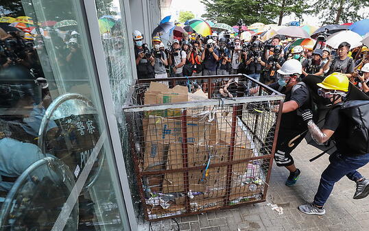 Mit einem Rollwagen aus Metall zertrümmert eine Gruppe von Demnonstranten eine Scheibe und stürmt das Parlament in Hongkong.