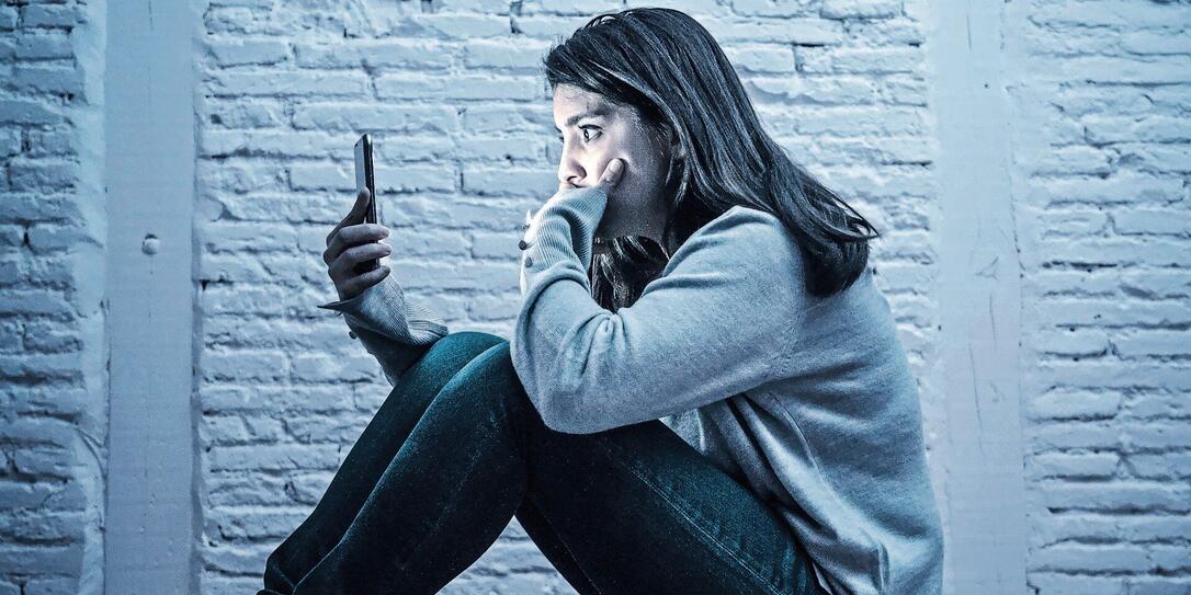 Portrait of sad scared young woman on the floor at night stressed and worried on smart mobile phone suffering cyber bullying harassment. desperate and depressed