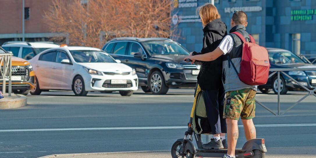 A young man and a girl on the same electric scooter at the intersection