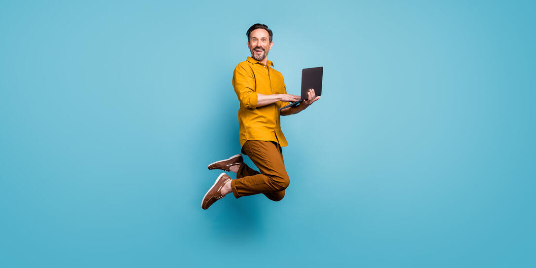 Full size photo of funky man feel rejoice emotions jump use laptop search social media online black friday discounts wear casual style clothing isolated over blue color background