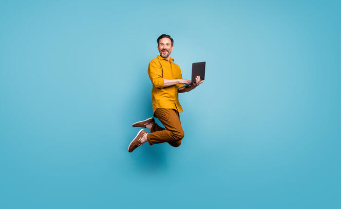 Full size photo of funky man feel rejoice emotions jump use laptop search social media online black friday discounts wear casual style clothing isolated over blue color background Full size photo of funky man feel rejoice emotions jump use laptop search social media online black friday discounts wear casual style clothing isolated over blue color background