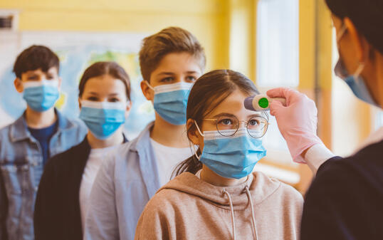 A teacher checks temperature of students at a high school