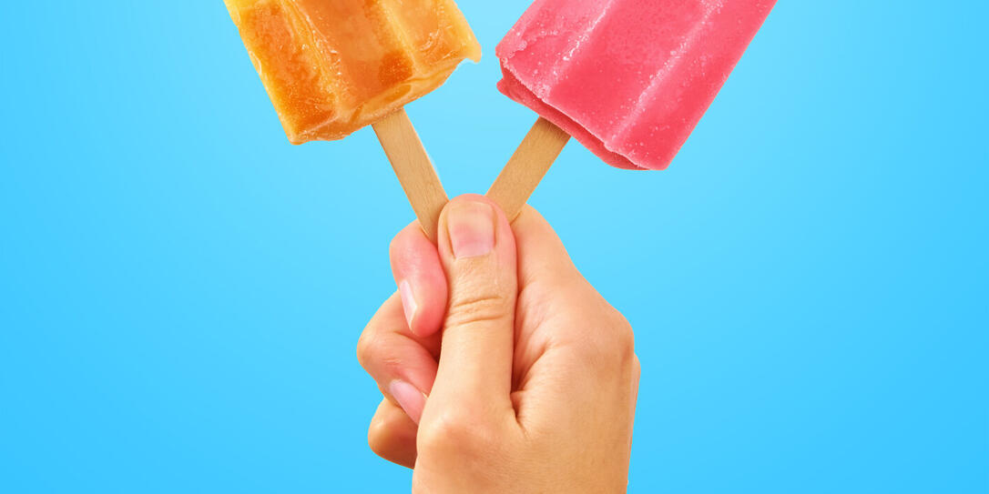 Two color popsicles in woman hands on blue background