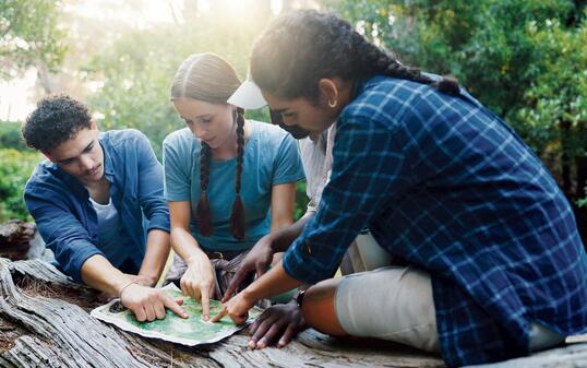Map, nature and group of friends hiking in forest with route plan for adventure together. Travel, outdoor and people with paper guide for trekking in woods on weekend trip for discovery or journey.