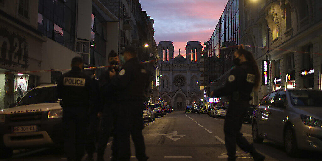 Polizisten gehen unter einem Absperrband vor der Kirche Notre Dame nach einem Messerangriff durch. Foto: Daniel Cole/AP/dpa