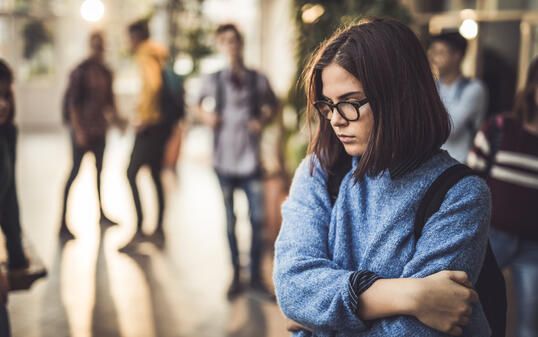 Sad high school student feeling lonely in a hallway.