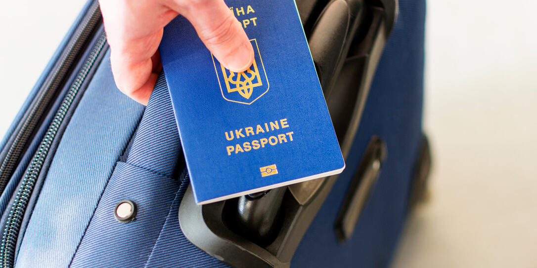 male hand holding a ukrainian passport above his luggage