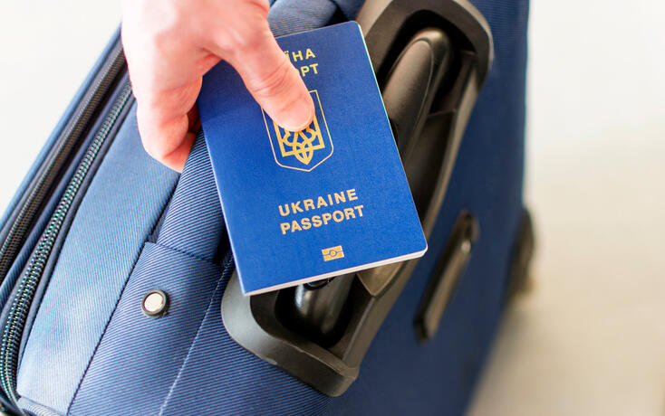 male hand holding a ukrainian passport above his luggage