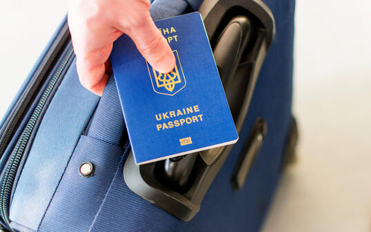 male hand holding a ukrainian passport above his luggage